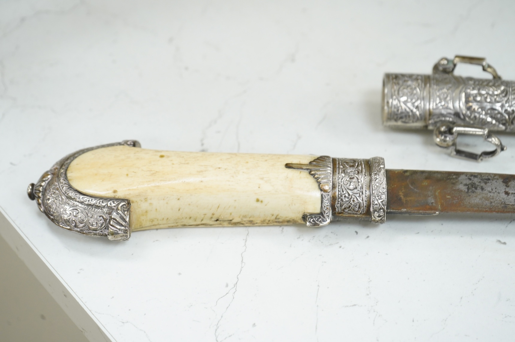 A silver mounted Moroccan dagger jambya, with silver sheath and hilt, mounts chased with foliate and floral designs, and one piece bone grip, blade as found, overall length 42cm
